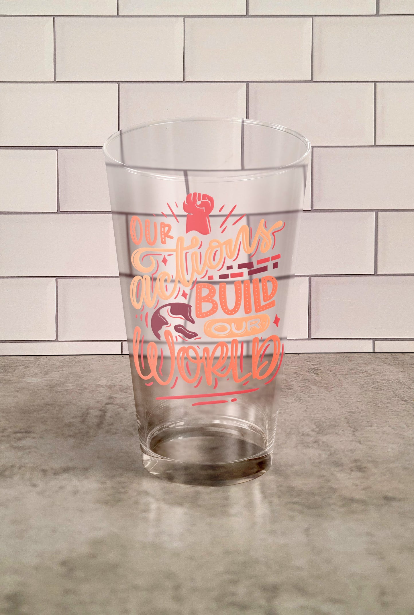 Our Actions Build Our World transparent Tumbler Glass against a slipslap wall