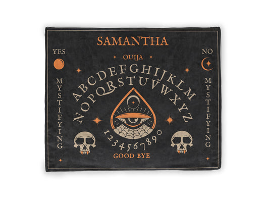 A Ouija board-themed throw blanket with intricate, full-color edge-to-edge printing featuring mystical symbols and letters. The blanket is laid out with a soft, cozy texture and a simple unprinted reverse side.