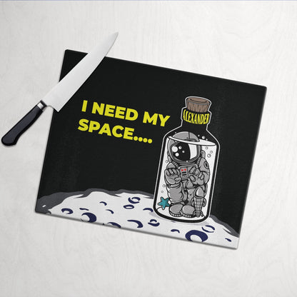 Glass cutting board with "I Need My Space" text, featuring an astronaut in a bottle labeled "Alexander," on a moon surface.