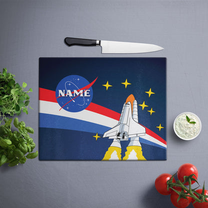 A glass cutting board with a lost in space design on a white wooden surface and knife on side